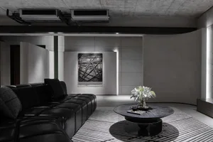 A modern living room with a black leather sectional sofa, abstract art, and a round wooden coffee table with a plant.