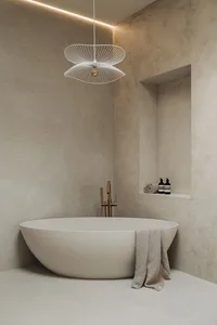 A minimalist bathroom interior with a freestanding bathtub, modern lighting fixture, and concrete walls.