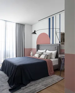 A minimalist bedroom featuring a grey bed with a pink accent wall and a modern floor lamp.