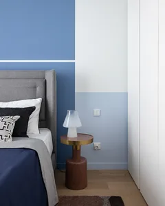 A minimalist bedroom featuring a bed with a wooden headboard and blue and white bedding, accompanied by a side table with a t