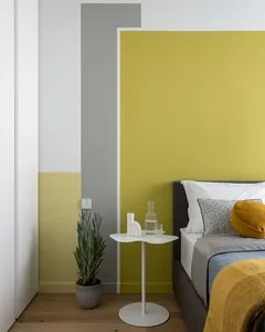 A minimalist bedroom featuring a bed against a wall painted in a gradient of yellow, grey, and white colors, with a small rou