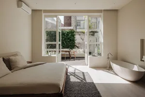 A modern bedroom with a large bed, free-standing bathtub, and large windows