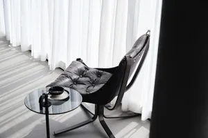 A sleek, modern leather chair with white cushions sits next to a round glass table with a mug and plate, against a backdrop o