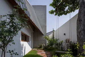 A modern private house with a concrete and glass exterior featuring a garden area and a tree.