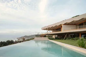 A modern residential house with a concrete exterior featuring a large outdoor infinity pool and ocean view.