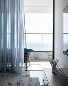 Modern residential space featuring glass, marble, and upholstered furniture with a view of the sea.
