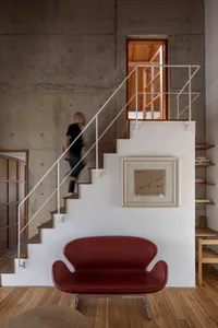 A contemporary living room with concrete walls, stairs, and a red sofa.