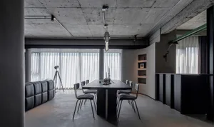 Industrial-style living and dining room with concrete flooring, black furniture, and white curtains.