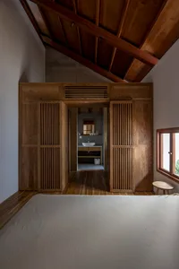 A minimalist bedroom featuring wooden elements, a wooden bed, and a wooden cabinet with a sink and mirror.