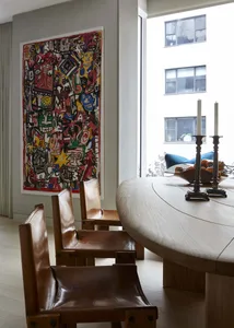 A modern dining room featuring a round wooden table with leather chairs and abstract art on the wall.