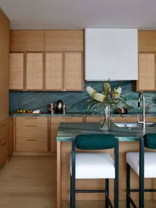 Modern kitchen featuring wooden cabinets with cane woven doors, green marble countertops and backsplash, and green upholstere