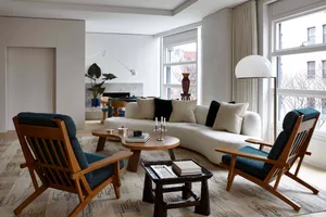 A modern living room featuring a curved white sofa, blue upholstered chairs, and a wooden coffee table with books and candles