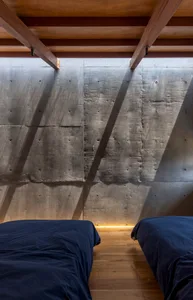 Two twin beds with dark blue sheets against a concrete wall with wooden beams and lights