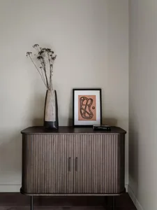 A minimalist cabinet with wooden doors and a vase with dried flowers.