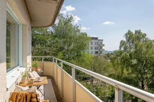 Modern residential balcony featuring a wooden table, white chairs, and green plants.