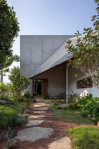 A modern residential exterior with a concrete facade, featuring a metal roof and a stone pathway.