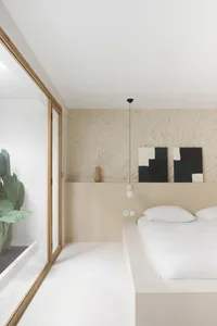 Minimalist bedroom with white walls, wooden flooring, and simple black and white artwork.