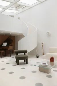 A minimalist interior space featuring a concrete floor with circular patterns and a spiral staircase.