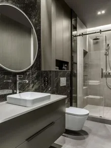 Modern bathroom designed with marble accents, featuring a floating sink, toilet, and glass-walled shower.