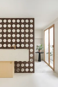 Modern bathroom with white marble sink and wood partition wall featuring circular cutouts.