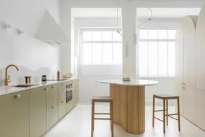 A modern kitchen with green cabinets, white countertops, and wooden stools.