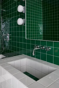 A modern bathroom with green-tiled walls, a white sink, and chrome fixtures.