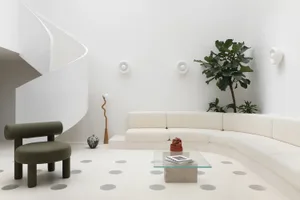 A modern minimalist living room featuring a white spiral staircase, a curved white sofa, a green armchair, and a glass coffee