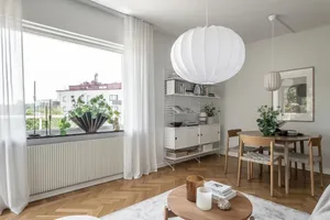 Modern minimalist living room showcasing wooden furniture, white pendant lights, and large windows.
