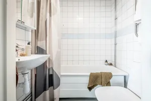 Minimalist bathroom with white ceramic tiles, a bathtub, a sink, and a shower curtain.
