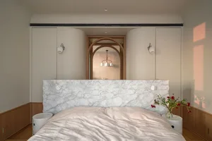 A minimalist bedroom featuring a marble bed with a white comforter, two bedside tables, and a wall-mounted light fixture.