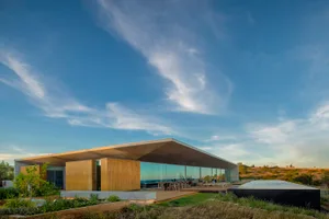 Modern building with glass exterior and metal roof, situated in a natural landscape.