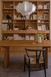 A modern home office featuring a wooden desk, chair, and bookshelves filled with books and decorative items.