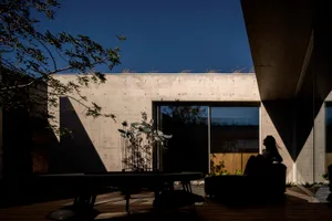 A modern interior space featuring a concrete wall and floor, with a person sitting in a minimalist outdoor area with a table 