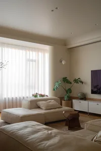 Modern minimalist living room with soft beige furniture, textured fabric, and a large flower arrangement in front of a window