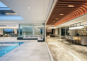 A modern, luxurious living room with a glass extension connecting to an outdoor pool area.