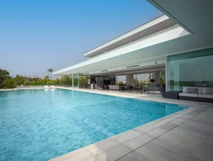 Modern living space featuring glass walls and marble finishes surrounded by a large swimming pool.