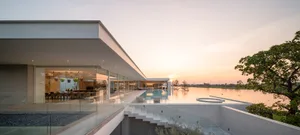 A modern residential building with glass walls and a rooftop pool overlooking a serene lake.