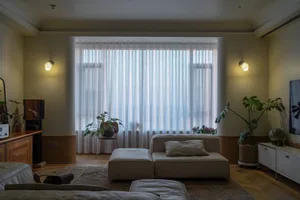 A modern living room featuring a beige sofa adorned with white cushions, positioned in front of a large window with sheer cur