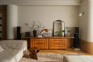A modern living room with wooden furniture, a white sofa, and a wooden sideboard with a vase and a cat.