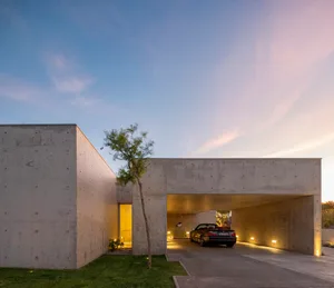 A modern, minimalist house with a concrete facade, featuring an indoor carport with a car parked inside.