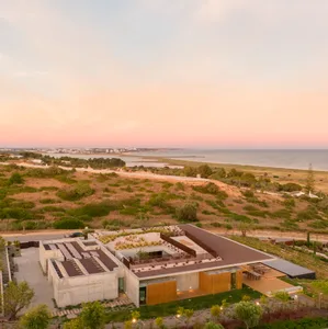 Modern house with concrete and wooden exterior against a scenic coastal backdrop at sunset.