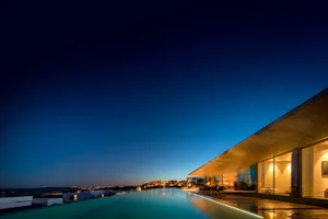 A modern residential home at night, featuring a glass and concrete exterior with an infinity pool.