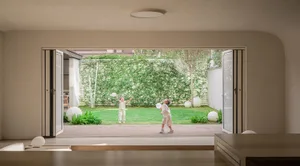 Two children playing badminton outdoors in a modern residential playarea with wooden deck and greenery.
