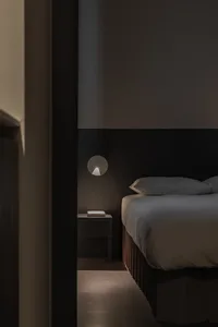 Minimalist bedroom with a bed made of textile material and a wall-mounted light fixture.