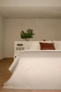 Minimalist bedroom with a white bed, wooden floor, and a green plant in a white pot.