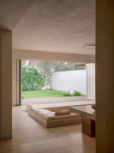 Minimalist living room with outdoor view, wooden floor, concrete walls, and glass walls.