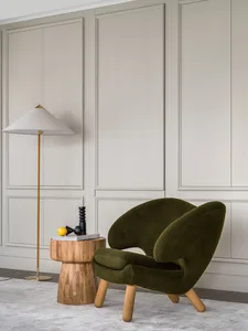 Modern, cushioned armchair with a greenish fabric upholstery and wooden legs, placed near a wooden side table with a floor la