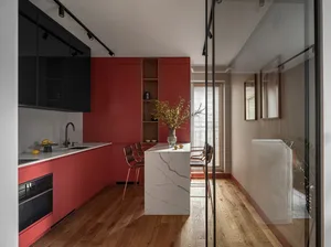 A modern kitchen featuring red cabinets, white marble top, and wooden flooring.