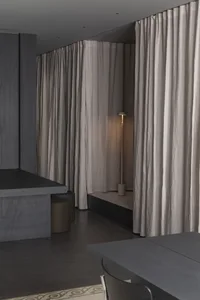 A minimalist room with concrete walls and floor, featuring a cushioned seat and a floor lamp.