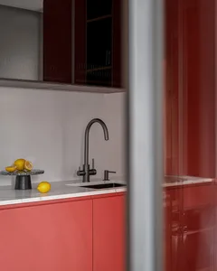 A modern kitchen with red cabinets, a white countertop, a black faucet, and lemons on a marble tray.